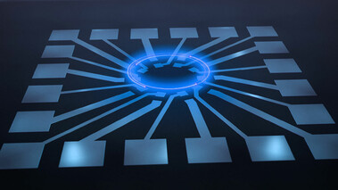 Schematische Darstellung eines Quantenbauteils mit zentraler blauer Leuchtstruktur auf schwarzem Hintergrund.